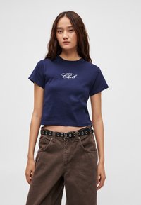 Tumši zila īsa kokvilnas T-krekls ar īsām piedurknēm un apaļu izgriezumu, uz krūtīm ar baltu uzrakstu "JOIN THE Club".