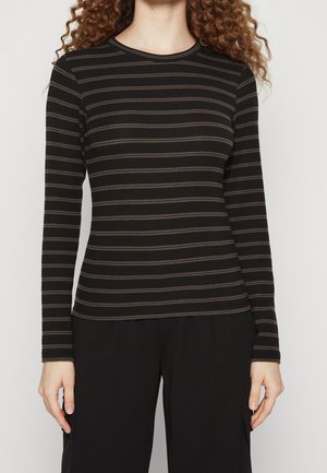 Femme portant un haut noir à manches longues avec de fines rayures grises horizontales et un pantalon noir, visible des épaules aux hanches.