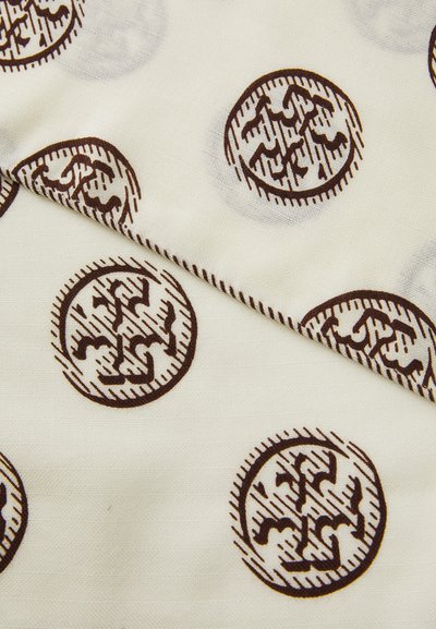 Balts audums ar atkārtotu brūnu aplīšu rakstu, kas ietver stilizētus dizainus. Auduma tekstūra šķiet gluda ar smalku spīdumu.