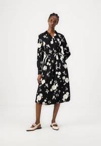 Μαύρο floral φόρεμα με λευκά σχέδια, μακριά μανίκια, κουμπί κλεισίματος και ζωνάκι στη μέση. Λεπτό ύφασμα με μήκος midi. Flat ροζ παπούτσια.