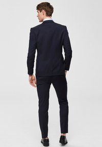 Marinblå skräddarsydd kavaj med tvåknappsstängning, matchande slim-fit byxor och svarta dresskor, med en slät tygtextur.