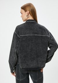Svart denimjacka med en avslappnad passform, vita sömnadsdetaljer och en minimalistisk design, med klassisk krage och knappmanchetter.