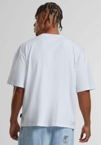 White short-sleeve t-shirt with a loose fit, crew neck, and smooth cotton texture. Features a small brand label on the lower left side.