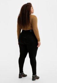 Leggings negros de talle alto con una textura suave, combinados con una parte superior ajustada de canalé mostaza de manga larga y botas negras hasta el tobillo.