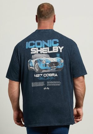 Homme portant un t-shirt bleu marine avec un motif voiture Shelby 427 Cobra bleu et blanc et du texte dans le dos.