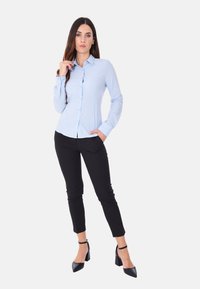Camicia azzurra chiara con un design aderente, abbinata a pantaloni neri a sigaretta. Accompagnata da scarpe nere con tacco alto e cinturini alla caviglia.