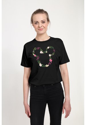 T-shirt noir à design floral en forme de cœur, avec des feuilles vertes et des fleurs roses et blanches. Manches courtes, coupe décontractée.