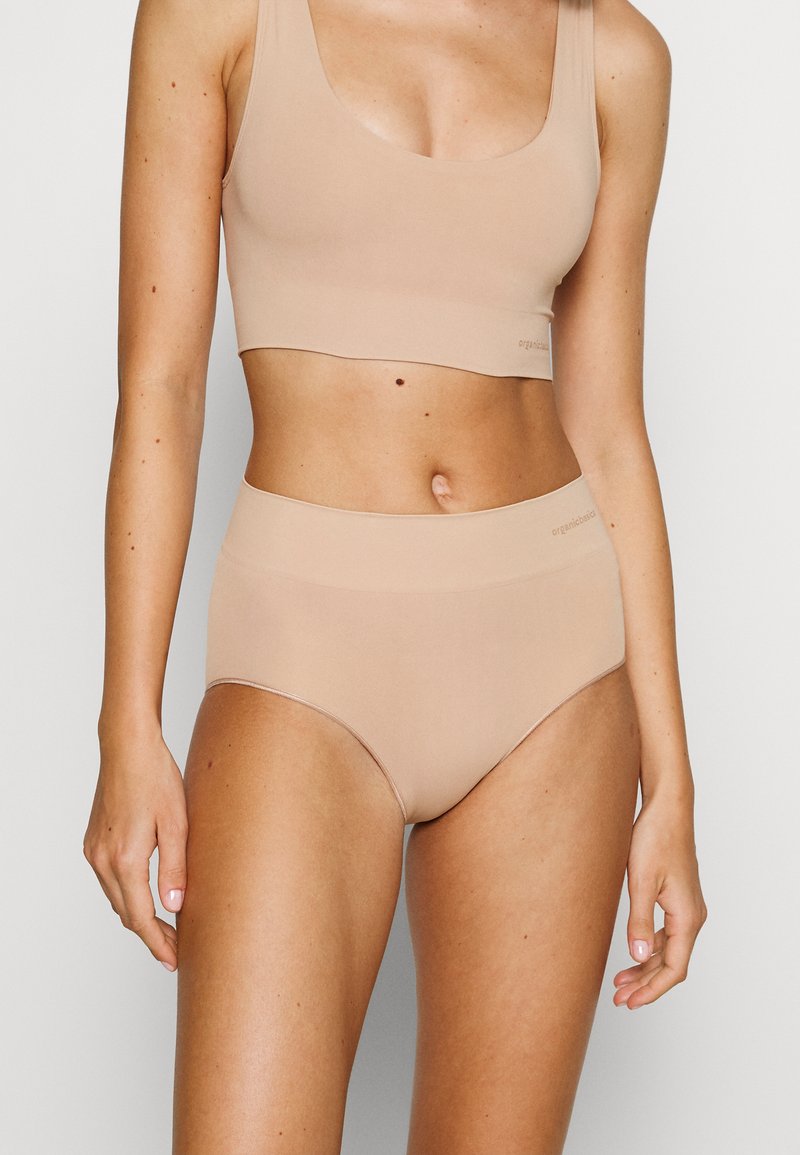 Beige bralette en hooggewaisted slip gemaakt van gladde stof, met een naadloos ontwerp en subtiele logo-details op de tailleband.