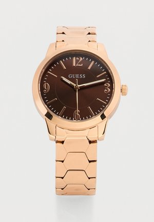 Roségouden metalen polshorloge met een donkerbruine wijzerplaat, gouden uurmarkeringen, drie wijzers en het GUESS-logo op de wijzerplaat.