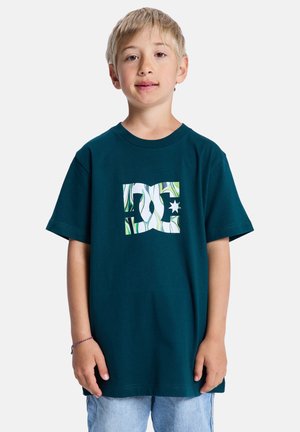 Tajemniczy bawełniany t-shirt w kolorze morskim z dużym białym logo DC z zielonymi i wzorzystymi akcentami. Krótkie rękawy i okrągły dekolt. Luźny, codzienny krój.