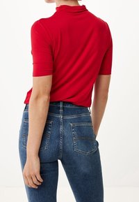 Röd kortärmad topp med hög halsdesign, ihop med högmidjade blå denimjeans med bakfickor och ljusa sömmar.