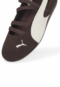 Καφέ αθλητικό παπούτσι σουέντ με λευκή δερμάτινη λεπτομέρεια, τέσσερις υφασμένες λουρίδες και ένα μικρό, κεντημένο λογότυπο στο πλάι.