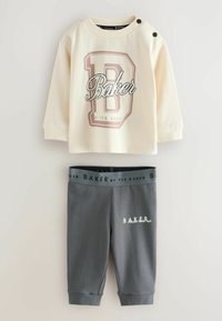 Cremefarbener Sweatshirt mit "Baker"-Logo und Schulterknöpfen, kombiniert mit grauen Leggings mit Logo-Bund und besticktem Detail.