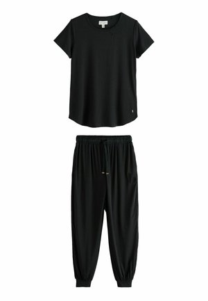Nahaufnahme einer Hand einer Person in der Tasche einer schwarzen Hose mit einem kleinen gestickten Buchstaben "b" in der Nähe der Tasche.