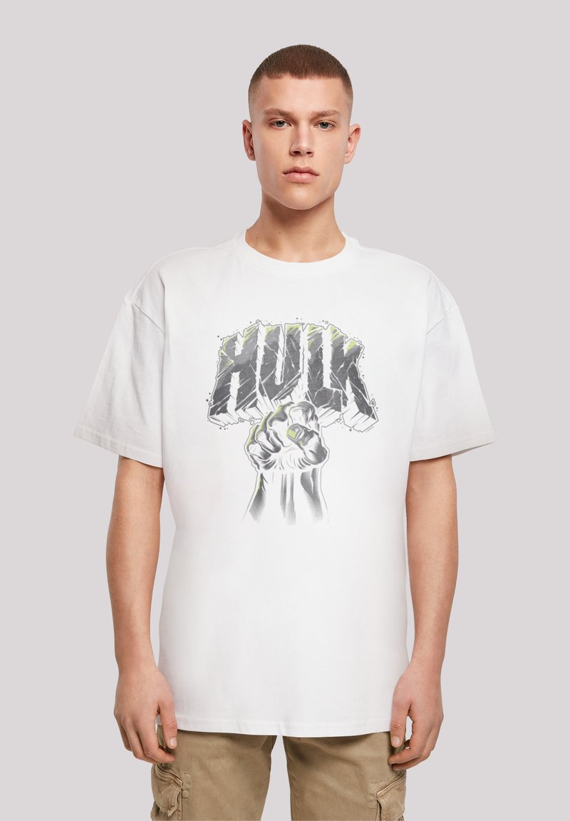 Hvit bomulls t-skjorte med et grafisk motiv av en knyttet neve og "HULK"-tekst i grått med grønne detaljer. Korte ermer og avslappet passform.