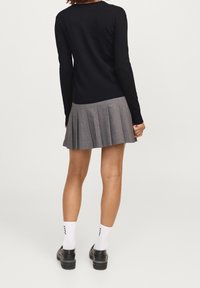 Svart långärmad tröja i kombination med en grå veckad kjol. Skorna är svarta med tjock sula och vita strumpor som visar varumärke.