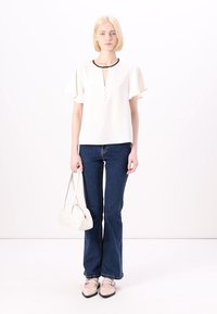Top bianco con maniche corte arricciate, scollo a V e bottoni decorativi. Abbinato a jeans svasati in denim scuro e scarpe beige.