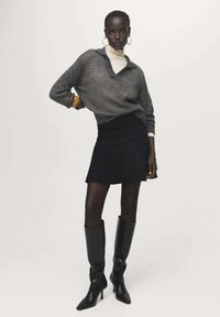 Prevelik sivi pleteni pulover s V-izrezom, složen preko bijelog turtleneck majice, u kombinaciji s crnom mini suknjom i crnim kožnim čizmama do koljena.
