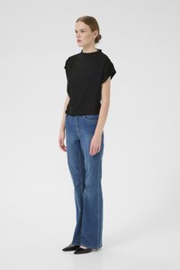 Haut noir à manches courtes associé à un jean bleu évasé taille haute, accentué par des ballerines noires pointues, sur un fond blanc uni.