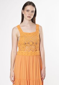 Orange kjole med en hæklede overdel med geometriske mønstre, firkantet udskæring og flydende, plisseret nederdel. Glat tekstur gennem hele kjolen.