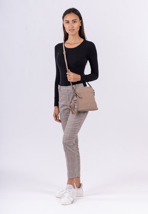 Haut noir à manches longues, pantalon à carreaux beiges et marron, associé à des baskets blanches et un petit sac beige avec un accent de pompon.