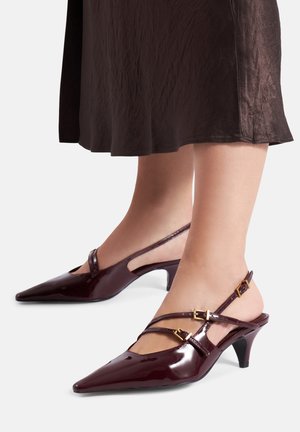 Tacones slingback de charol burdeos con puntera puntiaguda, correas ajustables con herrajes dorados y diseño de tacón bajo de tipo kitten.