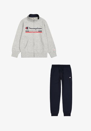Giacca zip grigia con logo, dettagli blu navy e due tasche; abbinata a pantaloni sportivi blu navy con coulisse regolabile e logo.