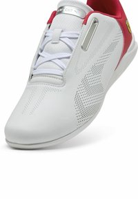 Scarpa sportiva bianca con accenti rosa, realizzata in materiale perforato, suola piatta, lacci spessi e un accento logo argento sulla linguetta.