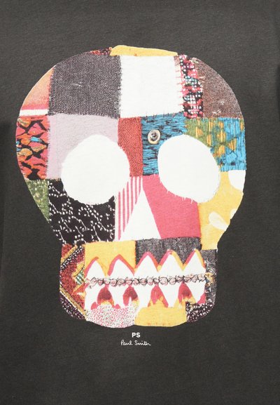 Έγχρωμο κρανίο παζλ με ποικίλα υφασμάτινα σχέδια και μάτι από κουμπί σε σκοτεινό φόντο, με την ένδειξη «PS Paul Smith» από κάτω.