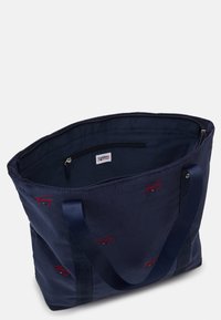 Sac fourre-tout en tissu côtelé bleu marine avec broderie de logo rouge, doubles poignées en tissu, poche intérieure zippée et design spacieux.
