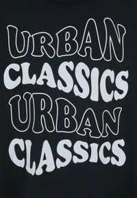 Melnas audums ar lieliem baltiem burtiem, kas lasāmi kā "URBAN CLASSICS" viļņotā, izkropļotā fontā, ar atkārtotām rakstu formām.