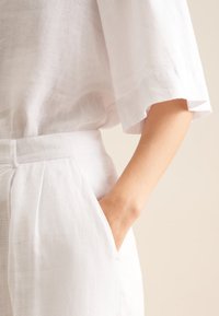 Een close-up van een hand die rust in de zak van lichte, kreukelige linnen kleding, wat een ontspannen modestijl toont.
