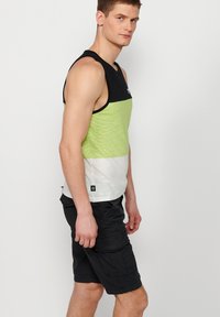 Juodas ir limonado žalias rankovės marškinėlis su baltu apatine dalimi, tekstūruota medžiaga ir logotipas ant krūtinės, derinamas su juodais k Cargo šortais.
