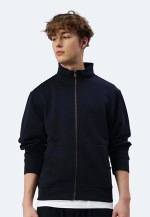 Felpa con zip di colore navy, colletto alto, polsini a costine e tasche laterali. Texture morbida, design minimale e dettaglio della zip dorata.