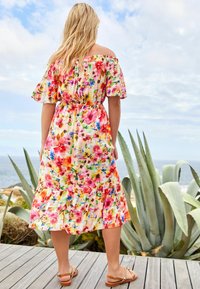 Robe fleurie à bretelles tombantes avec des fleurs colorées sur un fond clair, taille cintrée, jupe à volants, associée à des sandales légères.