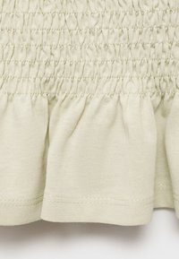 Svetlozelená zhrnutá tkanina s volánovým lemom, s textúrovaným, nariaseným dizajnom. Mäkký bavlnený materiál, jemne prešité okraje.