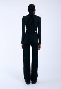 Black fitted long-sleeve top and high-waisted black wide-leg trousers, featuring textured fabric and back pockets. Model has long braided hair.