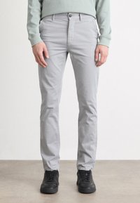 Jasnoszare chinosy o dopasowanym kroju, z zapięciem na guziki, szlufkami na pasek i kieszeniami. W zestawieniu z czarnymi trampkami na neutralnym tle.