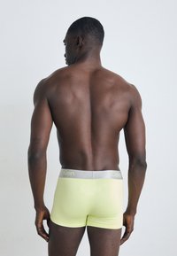 Calvin Klein boxershorts in lichtgeel met een zilveren tailleband. Gladde textuur en slanke pasvorm, gezien vanuit de achterkant.