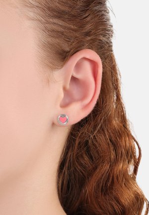 Silberne herzförmige Ohrstecker mit einem pinken Zentrum, die eine glatte metallische Oberfläche und ein kleines kreisförmiges Design aufweisen.