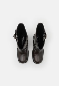 Botas de tobillo de cuero negro con un diseño elegante, que presentan un hebilla lateral y una textura lisa y brillante. Forma robusta de punta redonda.