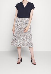 Haut bleu marine à manches courtes avec un col en V, associé à une jupe blanche ornée d'un motif léopard noir et marron. Des sandales à talons noires complètent le look.