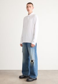 Hvit langermet polo skjorte kombinert med overdimensjonerte blåjeans med slitasjedetaljer, fullført med klumpete sorte støvler.