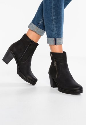 Botas negras hasta el tobillo con una textura de cuero suave, cremalleras laterales y un tacón cuadrado. Llevadas con unos vaqueros de mezclilla remangados.