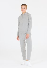 Szara bluza z kapturem z przednią kieszenią i regulowanym sznurkiem, zestawiona z dopasowanymi szarymi spodniami dresowymi z tapered, noszona z białymi sneakersami.