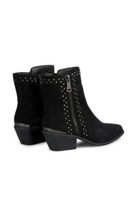 Schwarze Wildleder-Stiefeletten mit spitzer Zehe, seitlichem Reißverschluss und Nietenverzierungen entlang der Außennaht. Kleiner Absatz mit glänzendem Fußbett.
