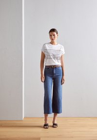 White t-shirt with navy horizontal stripes and sun graphic, paired with high-waisted, wide-legged blue jeans and black sandals.