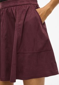 Jupe bordeaux en tissu doux, avec une taille froncée et des poches latérales. L'ourlet est légèrement évasé avec une texture lisse.