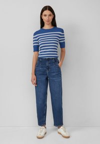 Maglione a maniche corte a righe blu, abbinato a jeans dritti a vita alta. Il modello indossa sneakers bianche con accenti beige.