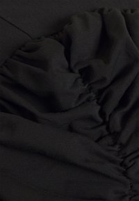 Black fabric close-up featuring gathered texture, smooth surface, and subtle sheen, showing a blend of fitted and loose elements.